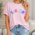 Person wearing a pink t-shirt with colorful text and blue jeans in a casual setting.