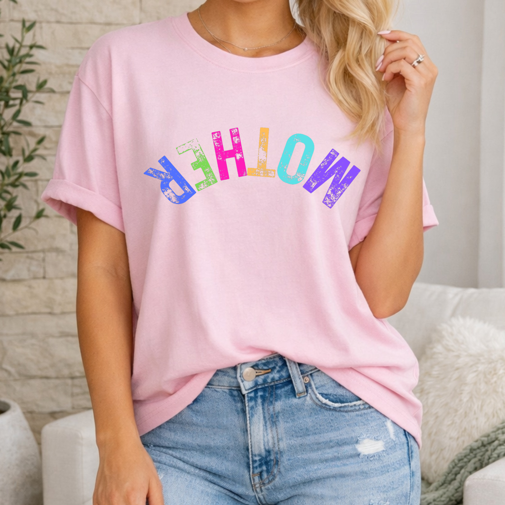 Person wearing a pink t-shirt with colorful text and blue jeans in a casual setting.